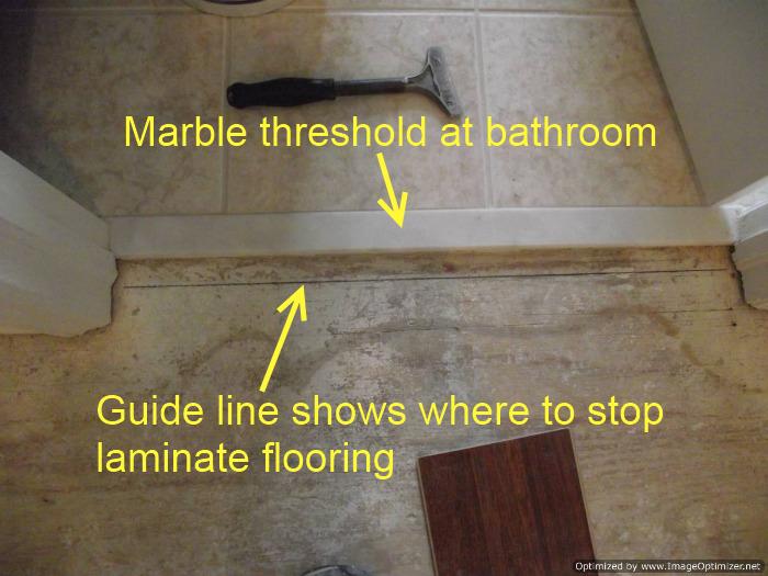 Installing laminate up to a marble threshold at a bathroom doorway, draw a guide line to show where to stop laminate flooring.